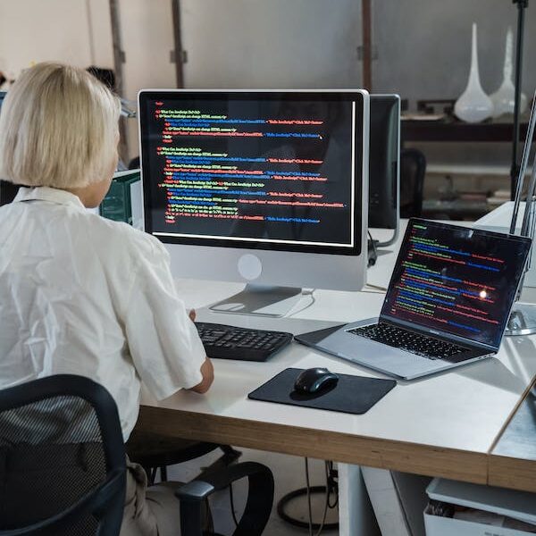 A profile shot of a woman with long brown hair, sitting at a wooden table at OpenText and laughing with someone not shown.